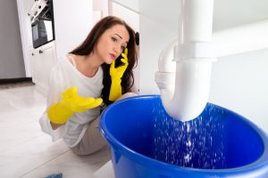 Upset Young Woman Calling Plumber To Fix Sink Pipe Leakage In Kitchen